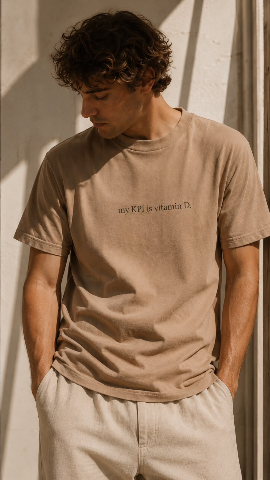 Man in the tan vitamin D tee leaning against a sunlit wall
